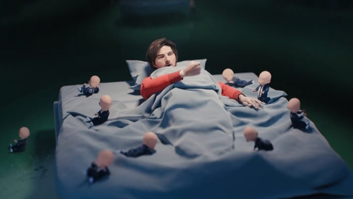 A screenshot from the opening credits of Severance, season 2, from Apple TV showing the protagonist lying on a bed, looking surprised, as numerous faceless babies surround him